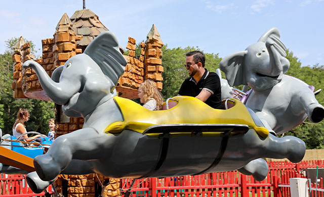 Man and young girl on flying elephant amusement ride